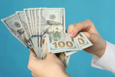 Turkuaz arka planda dolar sayan bir kadın, yakın plan. Para değişimi kavramı