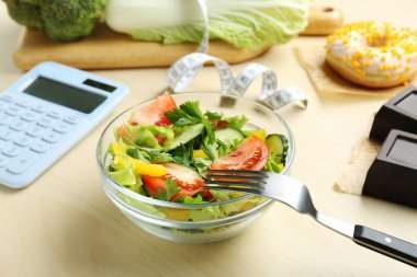 Hesap makinesi, kasede lezzetli salata ve ahşap masada diğer yiyecekler. Kilo verme konsepti