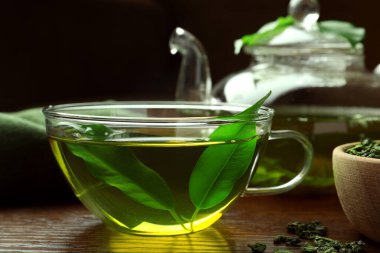 Cam bardakta taze yeşil çay, ahşap masada yapraklar, yakın plan.