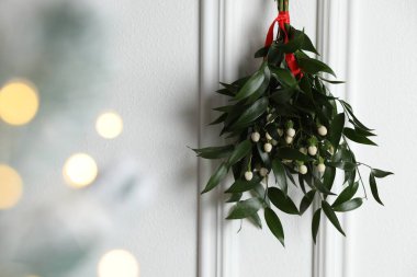 Mistletoe bunch with red ribbon hanging on light background, space for text. Bokeh effect clipart