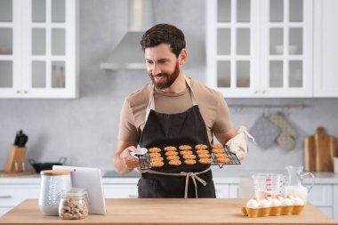 Mutfaktaki tabletten çevrimiçi aşçılık kursunu izlerken elinde taze kurabiyelerle ızgara tutan adam.