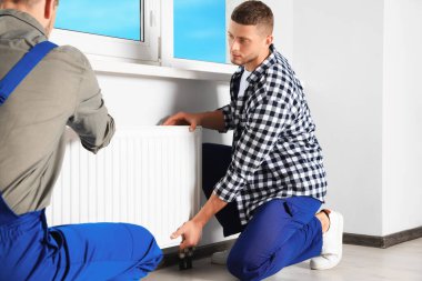 Professional plumbers installing new heating radiator in room