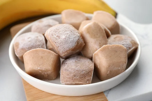 Frozen banana puree cubes and ingredient on light grey table, closeup