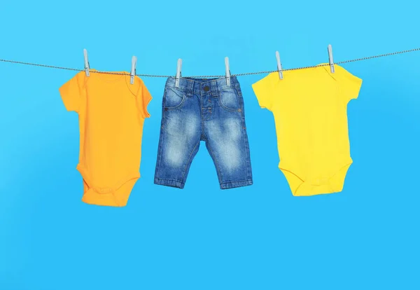 stock image Different baby clothes drying on laundry line against light blue background