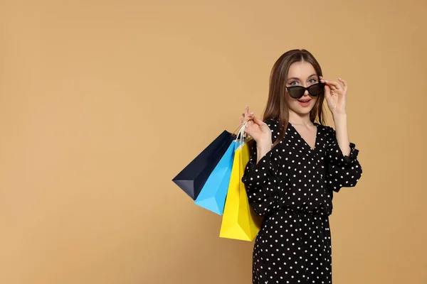 stock image Stylish young woman in sunglasses with shopping bags on beige background, space for text