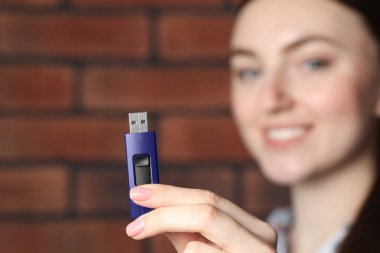 Kadın USB belleği tuğla duvarın yanında tutuyor, eline odaklan.