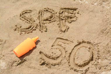 Kuma yazılmış SPF 50 kısaltması ve plajda boş bir güneş kremi şişesi.