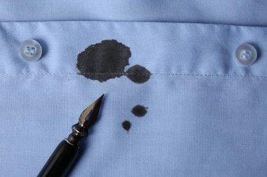 Açık mavi gömlek ve kalemle siyah mürekkep lekesi, üst manzara. Metin için boşluk