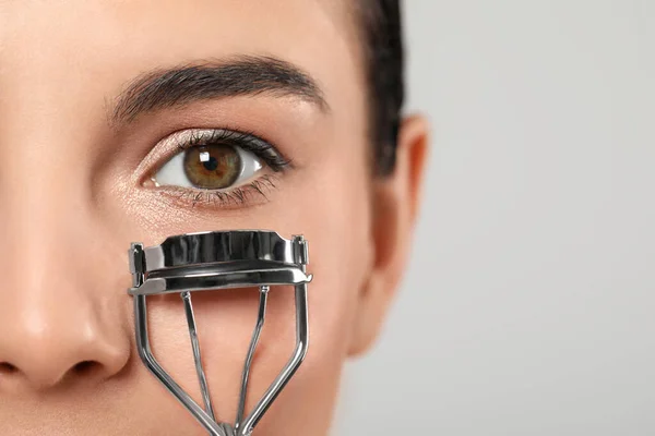 Young woman using eyelash curler on light grey background, closeup. Space for text