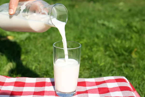 女性がボトルからグラスに新鮮な牛乳を注ぐチェッカーブランケット屋外でクローズアップ — ストック写真