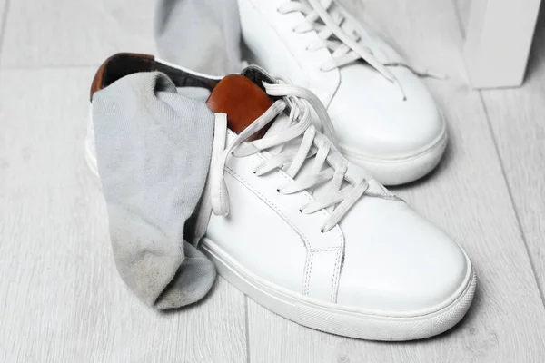 Sneakers with dirty socks on white wooden floor indoors