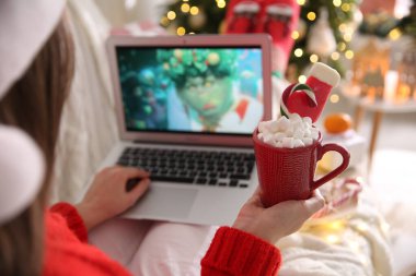 MYKOLAIV, UKRAINE - 25 Aralık 2020: Tatlı içkili kadın dizüstü bilgisayarında The Grinch filmini izliyor, yakın plan. Sıcak kış tatili atmosferi