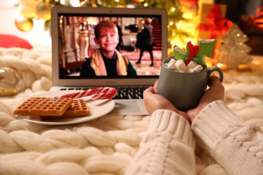 MYKOLAIV, UKRAINE - 23 Aralık 2020: Evde dizüstü bilgisayarda Evde Tek Başına filmi izleyen tatlı içkili kadın, yakın plan. Sıcak kış tatili atmosferi