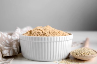 Kavanozda susam unu ve beyaz masada tahta kaşık tohum, yakın plan.