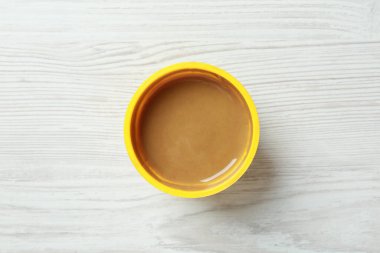 Beyaz ahşap masada plastik kabın içinde baharatlı hardal, üst manzara.