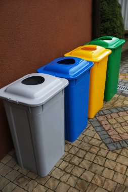 Açık havada kahverengi duvarın yanında birçok renk geri dönüşüm kutusu var.