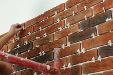 Profesyonel müteahhit duvara dekoratif tuğla yapıştırıyor, yakın plan. Döşeme kurulum süreci