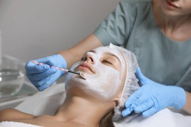 Spa salonu müşterinin yüzüne maske uygulayarak güzellik uzmanı