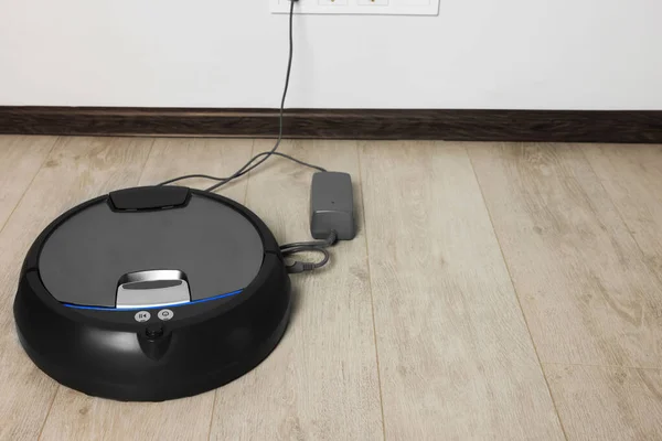 stock image Robotic vacuum cleaner charging on wooden floor near white wall, space for text