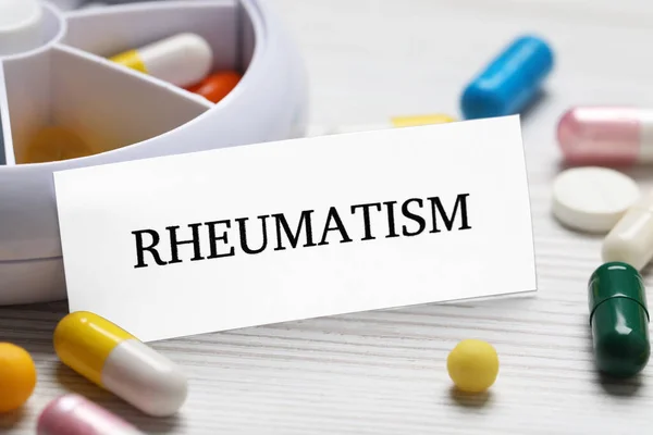 stock image Card with word Rheumatism and pills on white wooden table, closeup