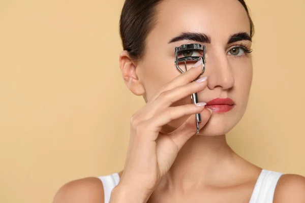 Woman using eyelash curler on beige background. Space for text