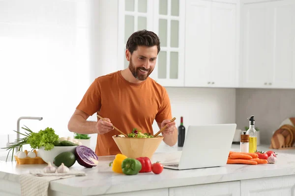 Człowiek Robi Kolację Podczas Oglądania Online Gotowania Kurs Pomocą Laptopa — Zdjęcie stockowe