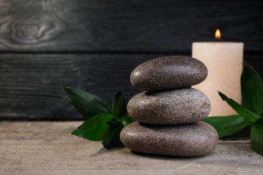 Tahta masaya istiflenmiş spa taşları, bambu ve mum. Metin için boşluk