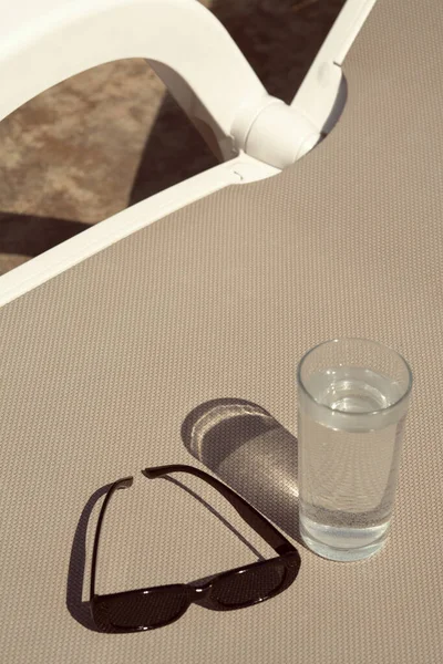 Stylowe Okulary Przeciwsłoneczne Szklanka Wody Szarym Leżaku Zewnątrz — Zdjęcie stockowe