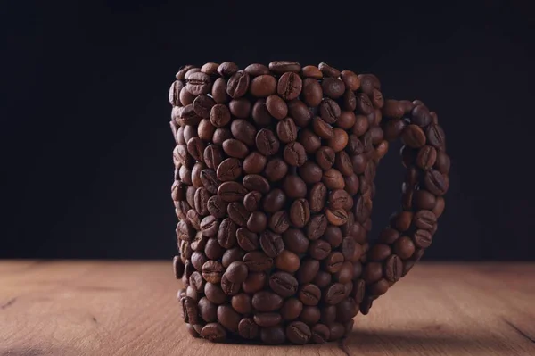 黒を背景に木製のテーブルの上にコーヒー豆で作られたカップ — ストック写真