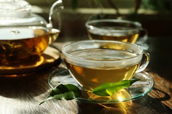 茶杯中的新鲜绿茶 木桌上有茶托 叶子和茶壶 — 图库照片