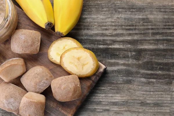 Frozen banana puree cubes and ingredient on wooden table, flat lay. Space for text
