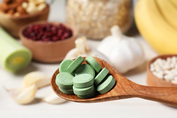 stock image Holding spoon of prebiotic pills near table with food, closeup