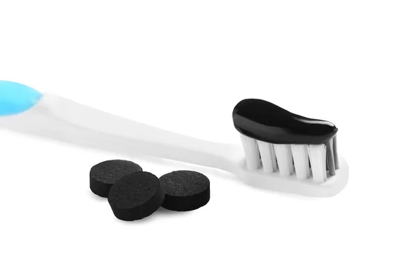 Brush with charcoal toothpaste and black pills on white background