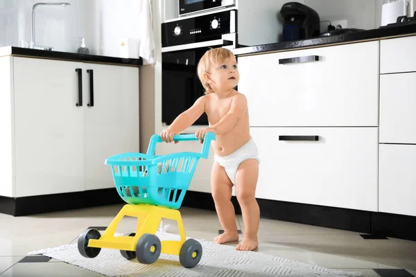 Cute baby making first steps with toy walker in kitchen. Learning to walk
