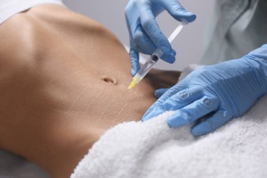 Genç bir kadın kuaförde göbek iğnesi yaptırıyor.