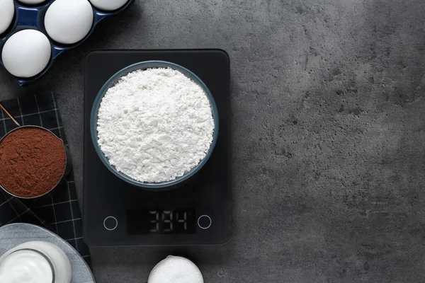 Electronic scales with flour and different products on grey table, flat lay. Space for text