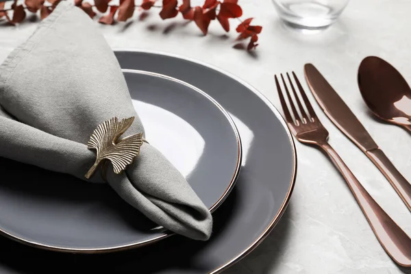 Plates with fabric napkin, decorative ring and cutlery on light gray marble table