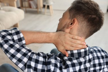 Man suffering from neck pain indoors, back view
