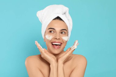 Duygusal genç bir kadın açık mavi arka planda kozmetik ürünlerle yüzünü yıkıyor.