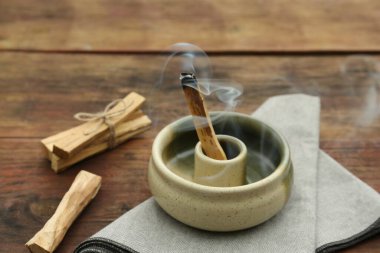 Palo Santo stick smoldering in holder on wooden table clipart