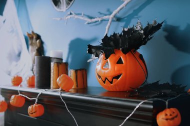 Mavi duvarın yanındaki ahşap şöminede fener ışıkları ve siyah akçaağaç yaprakları.