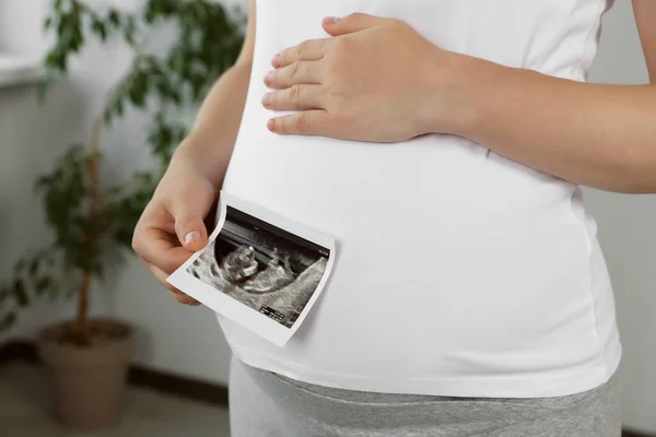 Pregnant woman with ultrasound picture of baby in room, closeup