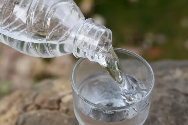 Pouring water from bottle into glass outdoors, closeup
