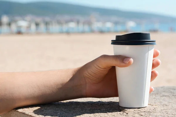 Woman with takeaway coffee cup on beach, closeup