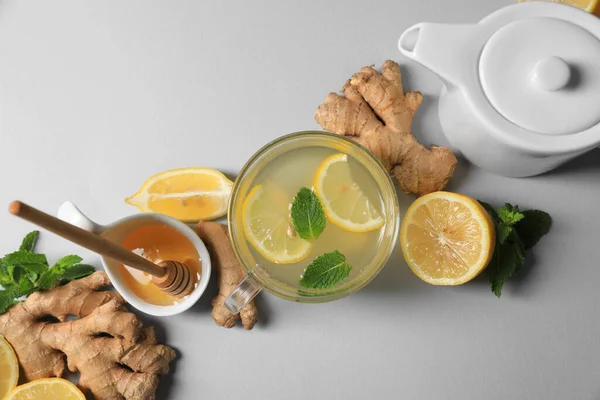 Delicious ginger tea and ingredients on light grey background, flat lay
