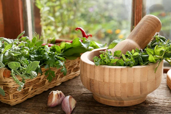 Mortar with pestle and fresh green herbs on wooden table