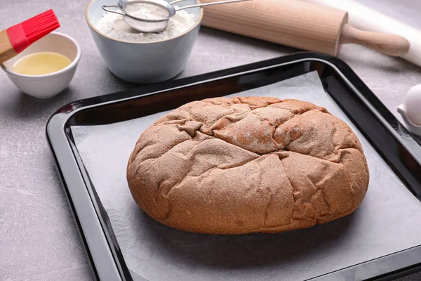 Baking pan with tasty homemade bread and parchment paper on light grey table