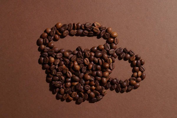 Cup of drink, composition made with coffee beans on brown background, flat lay