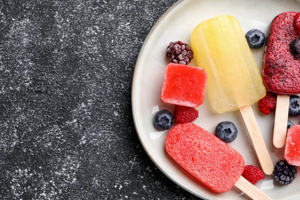 Plate of different fruit ice pops on black textured table, top view. Space for text