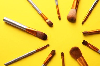 Sarı arka planda farklı makyaj fırçaları, düz yatış. Metin için boşluk